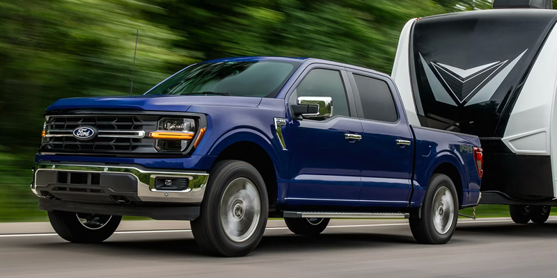 Blue Ford F-150 pickup truck towing a large travel trailer on a road