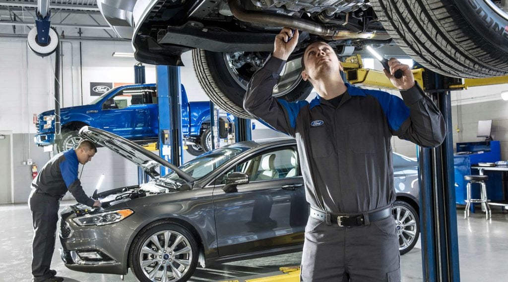 Automotive technicians inspecting and servicing vehicles inside a Ford service center.